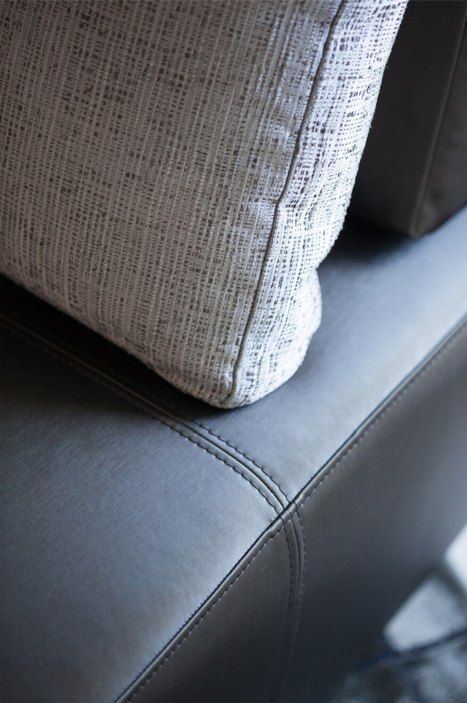 Grey textured fabric pillow with visible seam on Lucca Chair dark leather upholstery