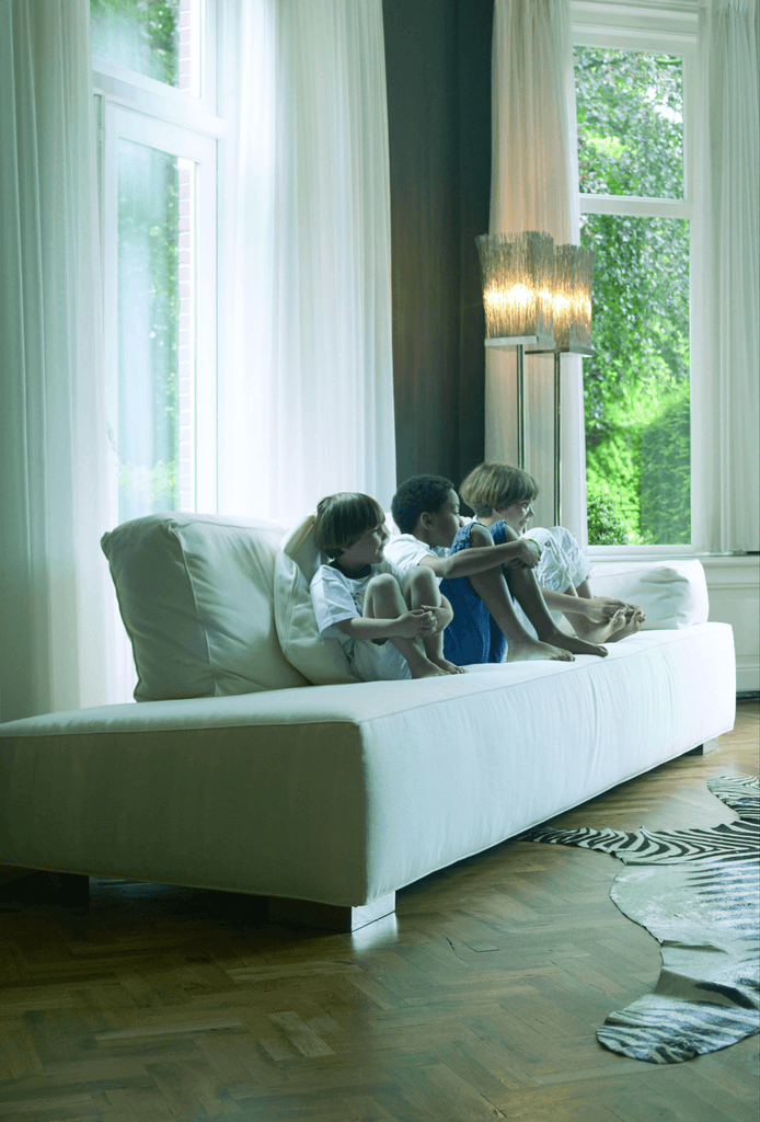 Three children sitting on a white sofa near a Broom Floor Lamp in a cozy living room