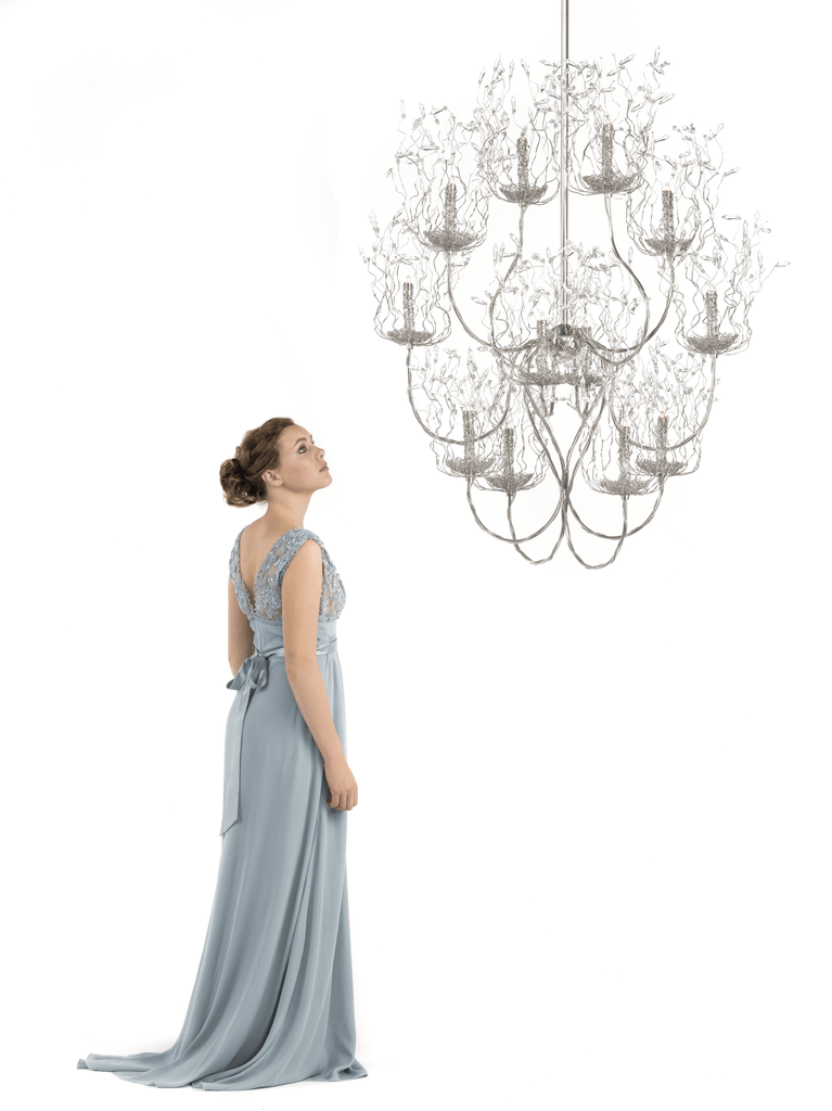 Woman in light blue gown gazing at ornate spirits chandelier round in luxurious setting